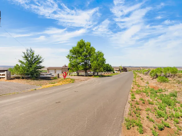 Paved road approaching a property with a visible garage structure and mature trees