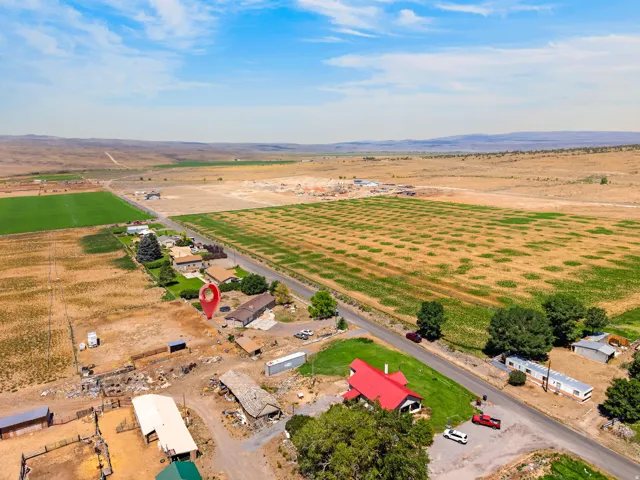 Aerial view of a rural property featuring a red-roofed building, multiple outbuildings, and agricultural fields
