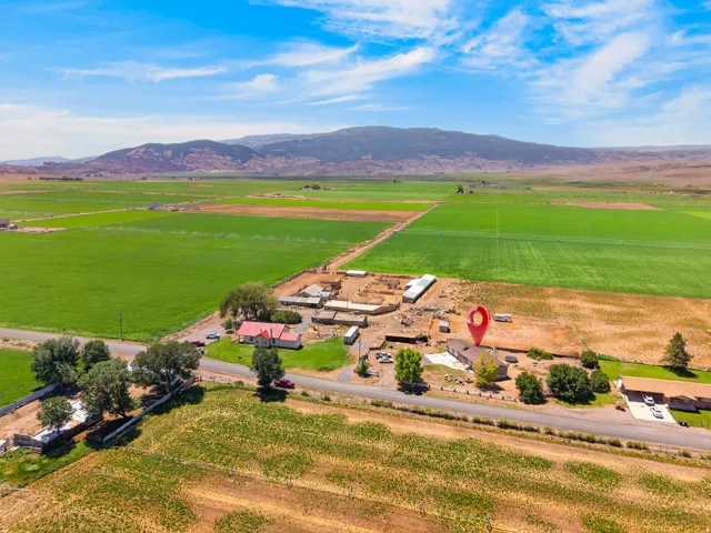 Rural property featuring a single-story residence, multiple outbuildings, and expansive green fields