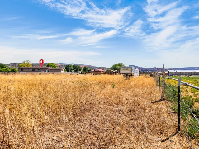 Expansive open field with natural vegetation, featuring perimeter fencing and distant structures