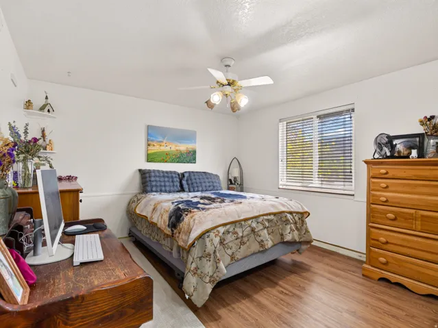 Bedroom featuring wood-finish flooring, a ceiling fan with integrated lighting, and a single window with horizontal blinds