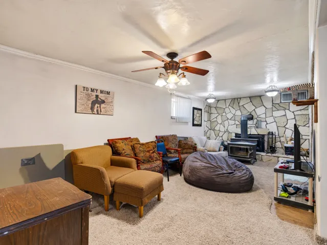 Spacious room featuring a stone accent wall with a wood-burning stove and a ceiling fan with integrated lighting