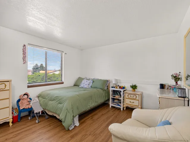 Bedroom featuring wood-finish flooring, a bright window with horizontal blinds, and a neutral wall color