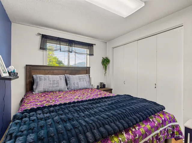 Room featuring a window with horizontal blinds, wood-finish headboard, built-in closet with bi-fold doors, and a ceiling-mounted fluorescent light fixture