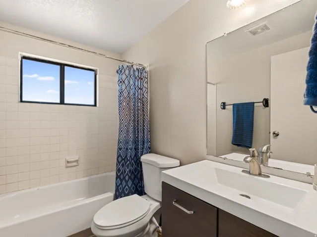 Bathroom featuring a modern vanity with integrated sink, brushed nickel faucet, a large wall-mounted mirror, a tub/shower combination with white tile surround, and a double-pane window