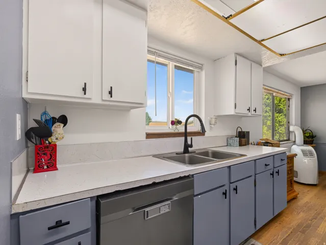 Kitchen featuring white upper cabinetry, gray lower cabinetry, a dual basin sink with a matte black faucet, and light-colored countertops