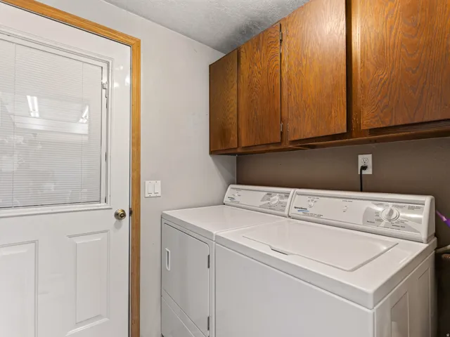 Dedicated laundry area featuring a white washer and dryer pair, wood cabinetry, and a white door with integrated blinds