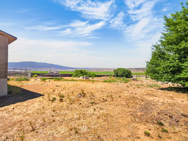 Expansive outdoor space featuring a brick structure, distant agricultural fields, mature trees, and a mountain backdrop