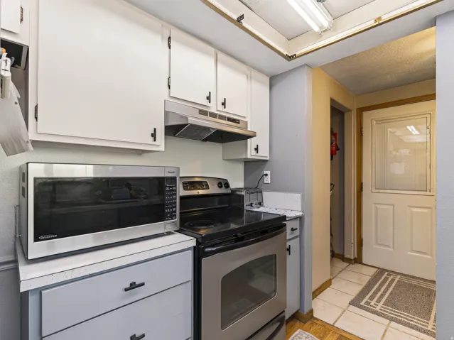 Kitchen featuring white upper cabinetry with black hardware, stainless steel range with oven, and a built-in exhaust hood