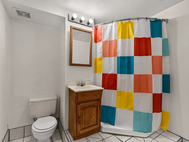 Bathroom featuring a shower stall with curved shower rod, a wood-finish vanity with an integrated sink, a wall-mounted mirror with wood framing, and a toilet