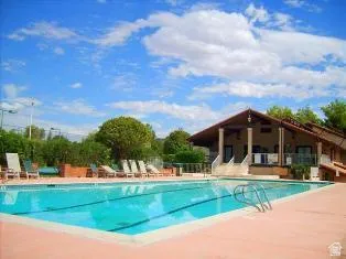 Large outdoor pool with integrated lane lines and a surrounding deck, complemented by a multi-level Club House featuring a covered patio with columns and a terra cotta tile roof