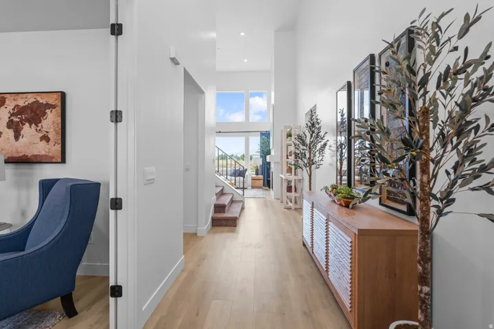 Spacious entryway featuring light wood-finish flooring, high ceilings, recessed lighting, a modern staircase with wrought iron railing, and upper-level windows providing natural illumination