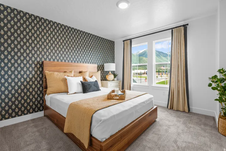 Bedroom featuring an accent wall with patterned wallpaper, light-colored carpeting, two windows, and a mountain backdrop