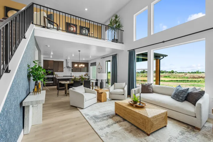 Vaulted ceiling living area featuring expansive windows, wood-finish flooring, and a second-story open-concept loft with a black metal railing