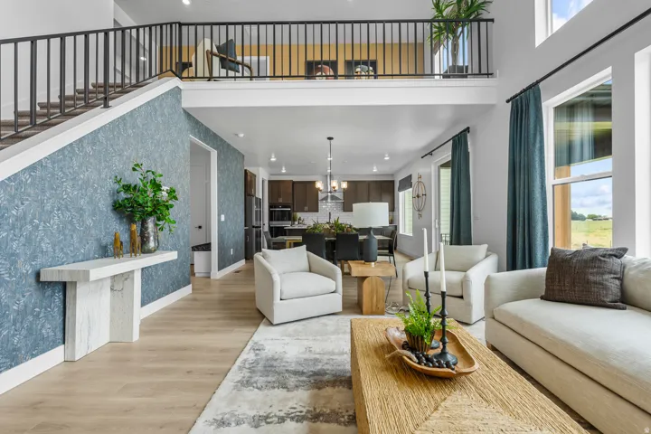 Two-story living area featuring a prominent staircase with a dark metal railing, wood-finish flooring, and a mezzanine balcony