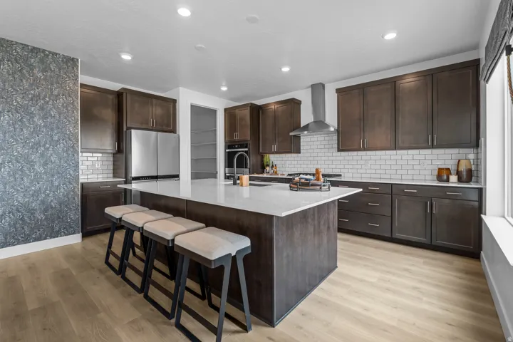 Spacious kitchen featuring a large central island with seating, stainless steel appliances, dark wood-finish cabinetry, white subway tile backsplash, and light wood-finish flooring
