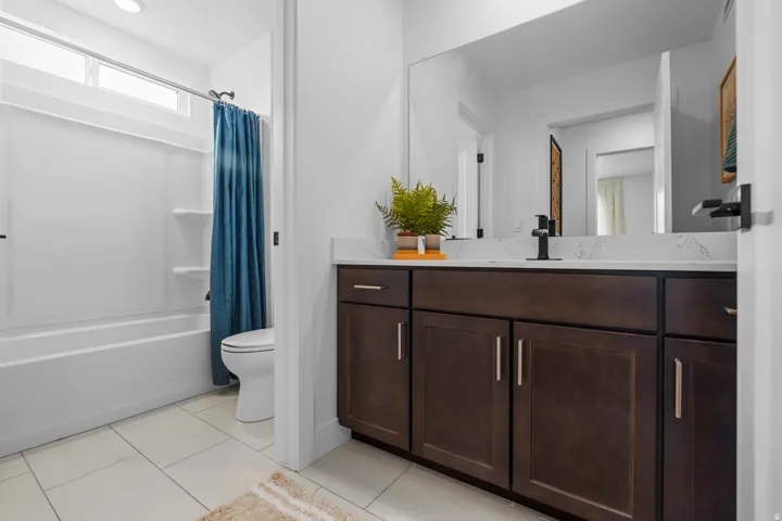 Bathroom featuring a dark wood-finish vanity with a light-toned countertop, a full-width mirror, and a white tub/shower combination with a transom window