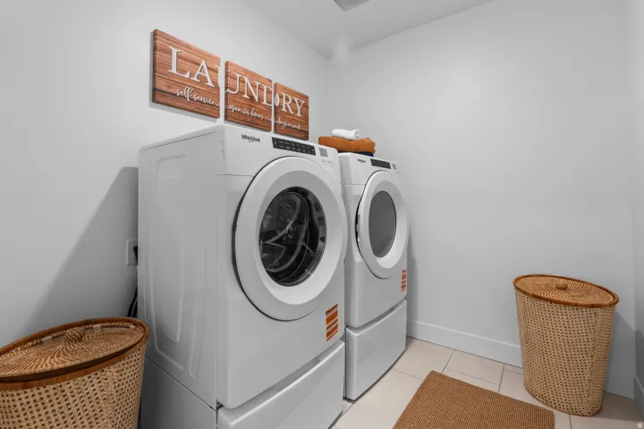 Dedicated laundry area featuring a front-loading washer and dryer set on pedestals, complete with a tiled floor and white wall finishes