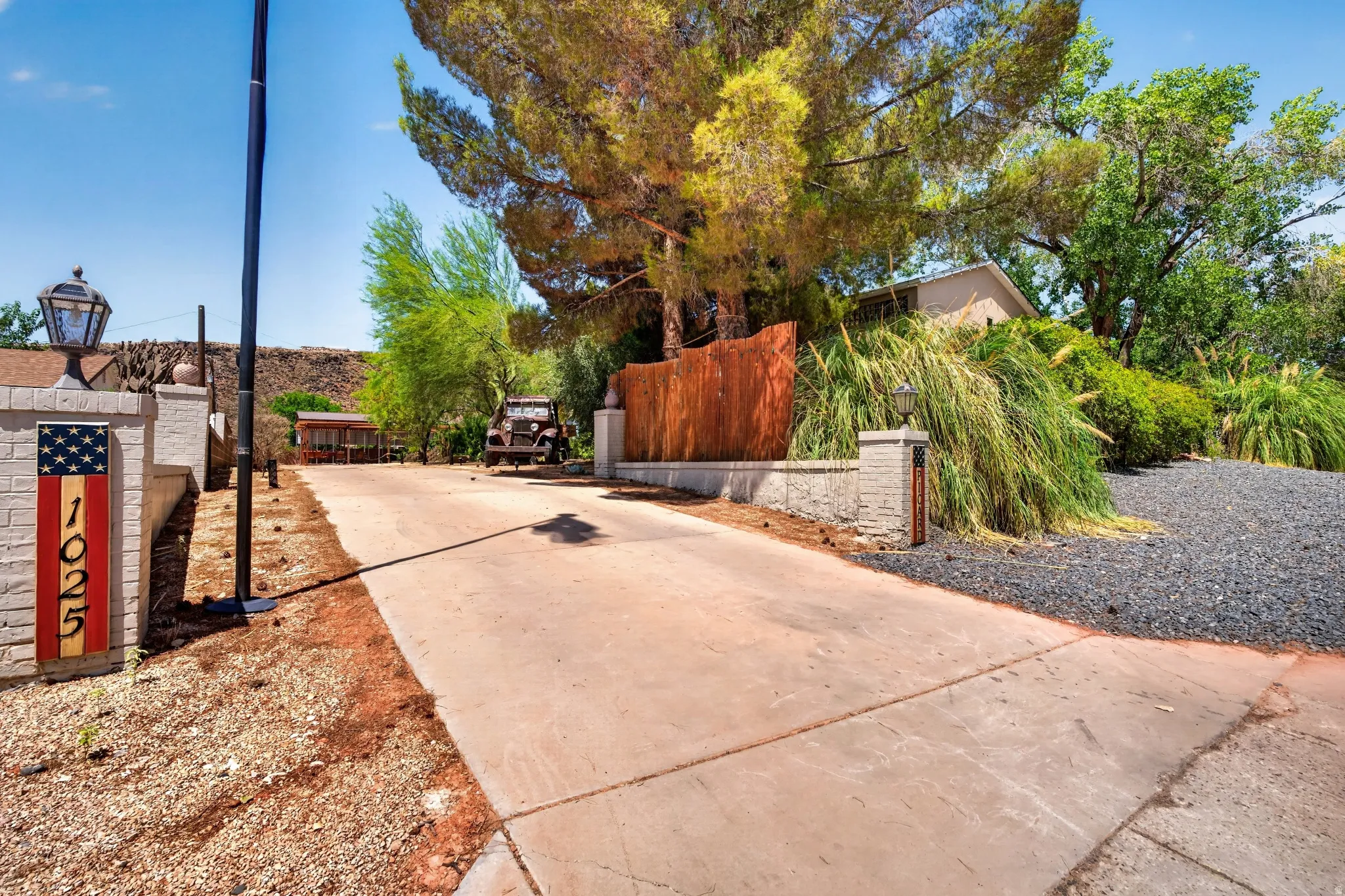 Gated entry with brick pillars, custom address marker, and a concrete driveway leading to the property