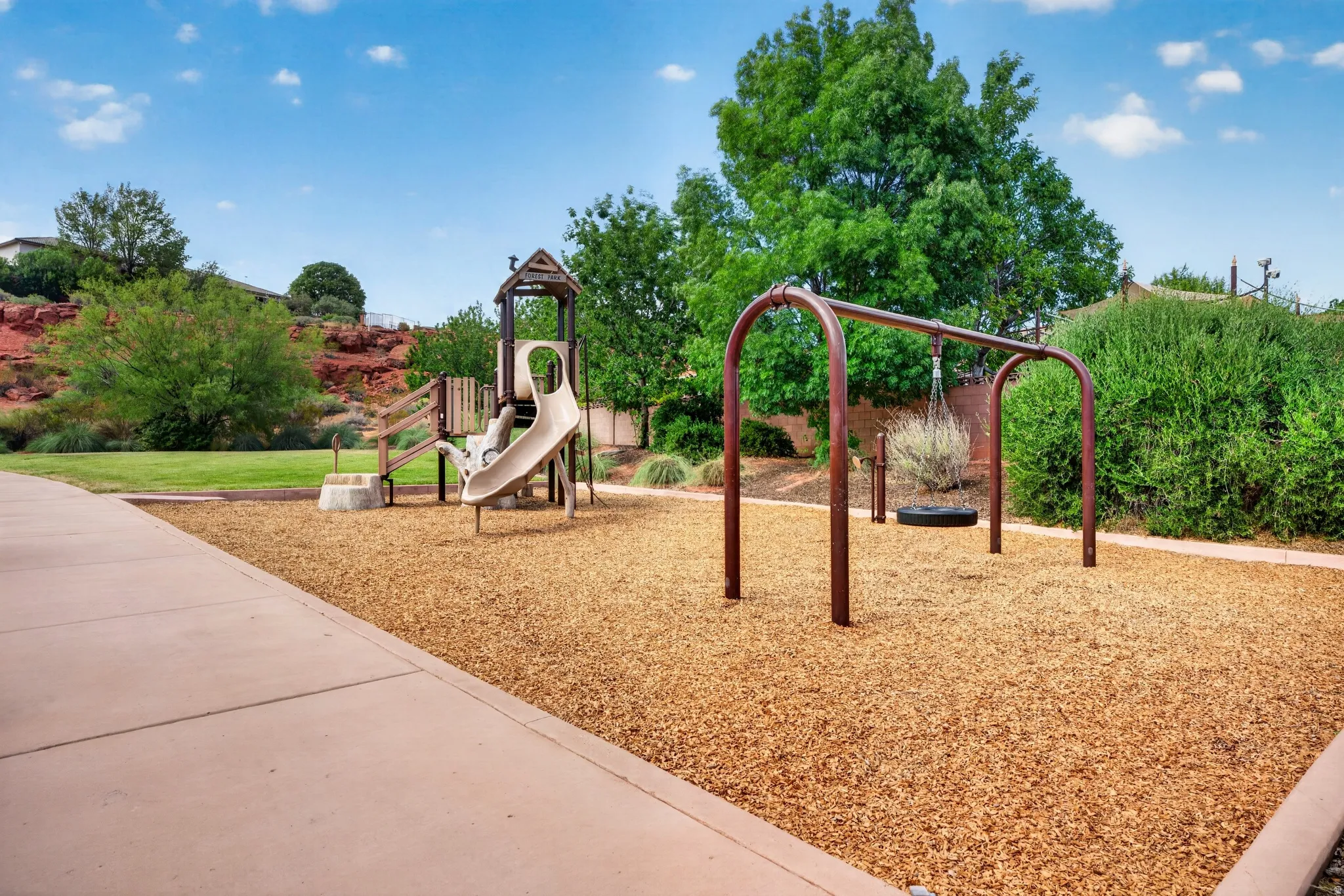 Outdoor recreational area featuring a playground structure with a slide, a swing set with a tire swing, and wood chip surfacing