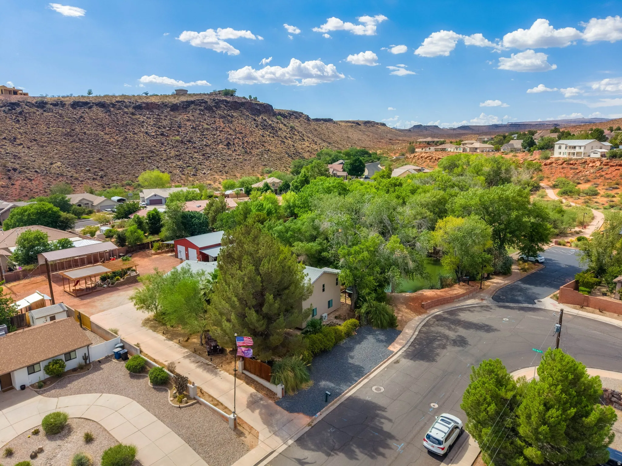 Aerial overview of a residential neighborhood with varied architecture, mature trees, and red rock geographical features