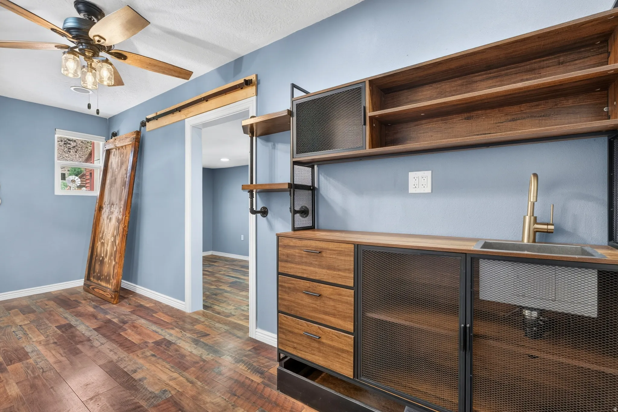 Built-in wet bar featuring wood-finish cabinetry, metal mesh doors, and a single basin sink with a gold-tone faucet