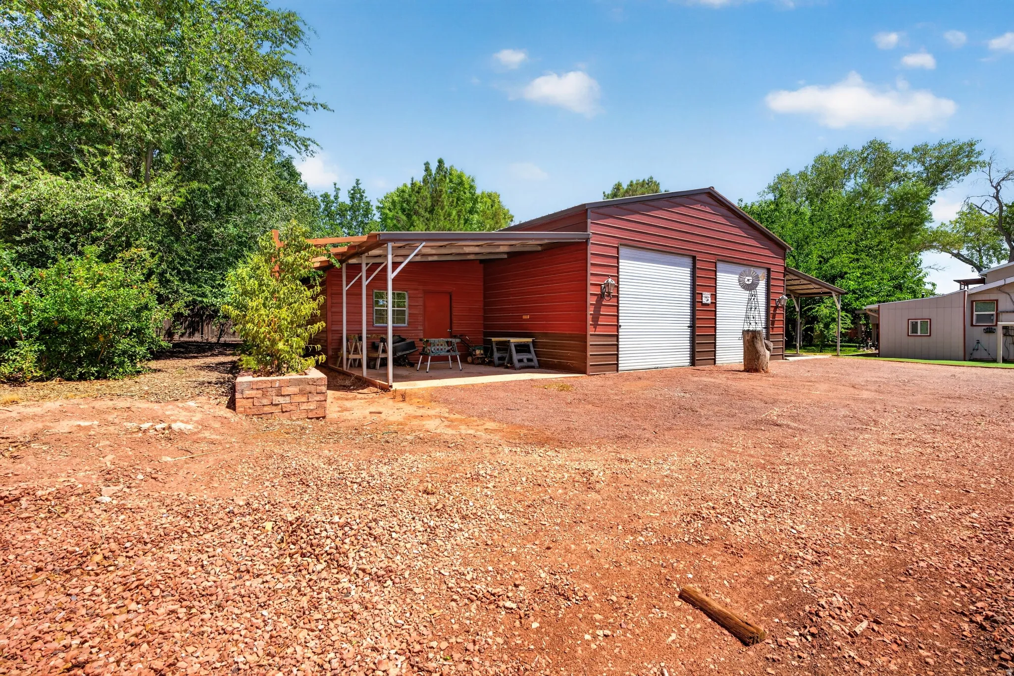 Red metal building featuring two garage doors, an extended covered patio, and a gravel-covered area