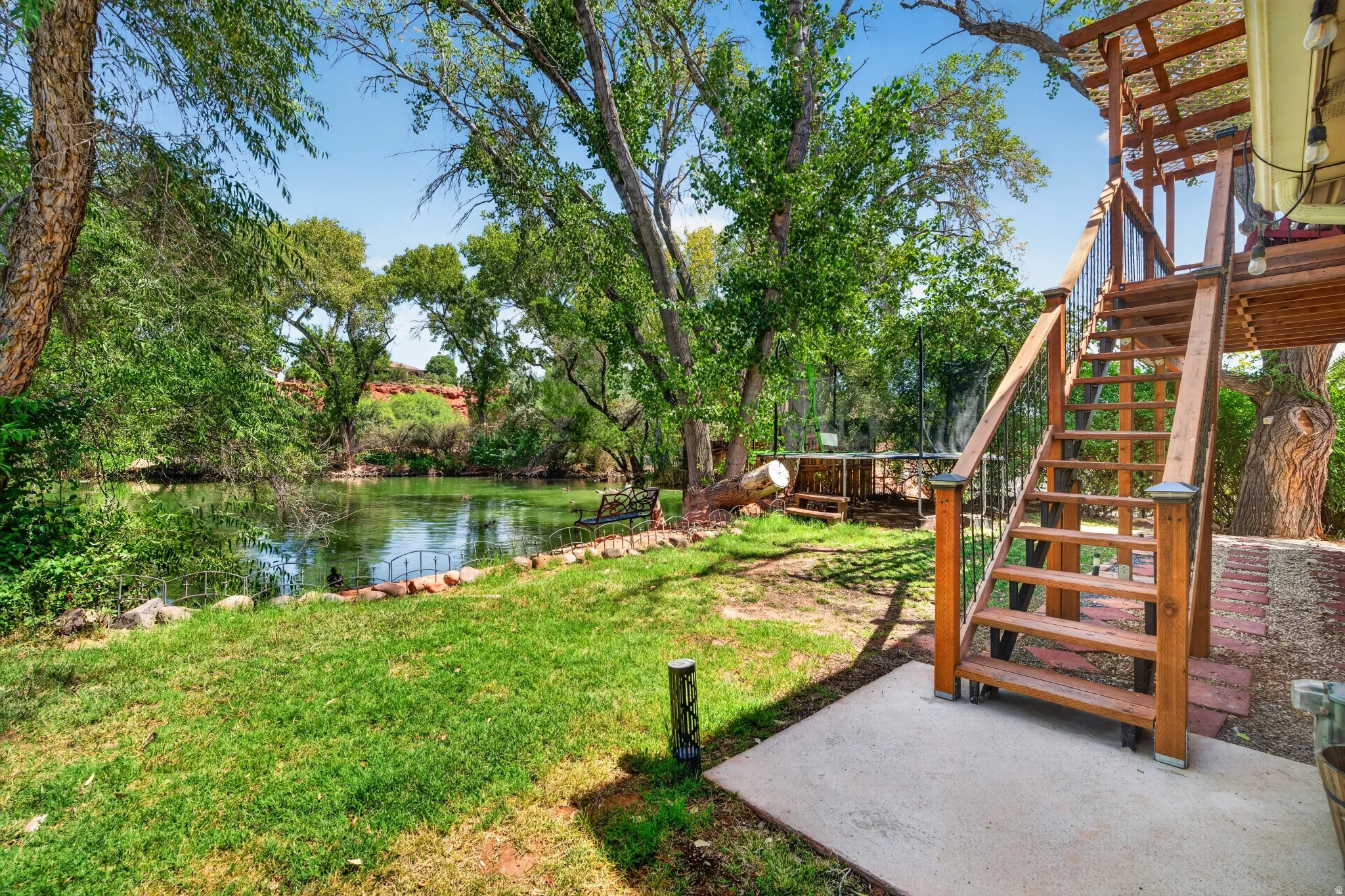 Lakeside property featuring a wooden staircase with metal balusters, a concrete pad, natural wood decking, and a stone-edged garden area