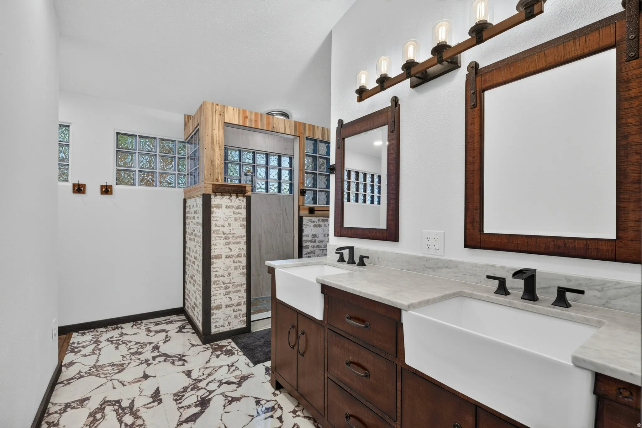 Dual farmhouse sinks set into a wood-finish vanity with a light-toned countertop