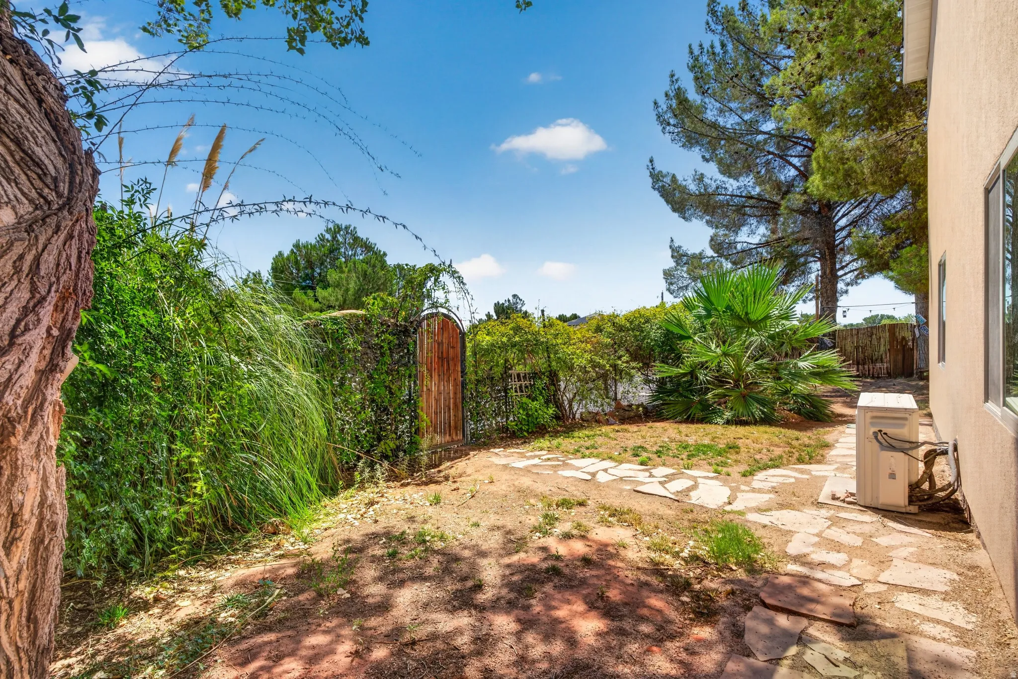 Expansive outdoor area featuring a stone pathway, established trees, mature landscaping, and a rustic wooden gate