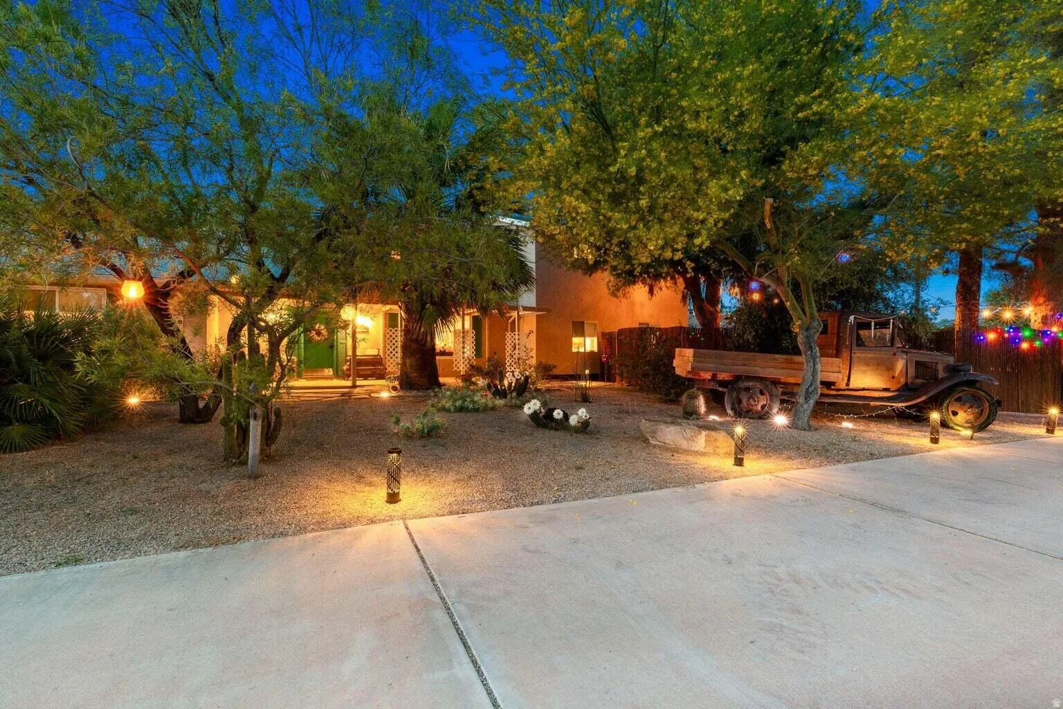 Low-maintenance gravel landscaping with mature trees, walkway lighting, and a concrete driveway