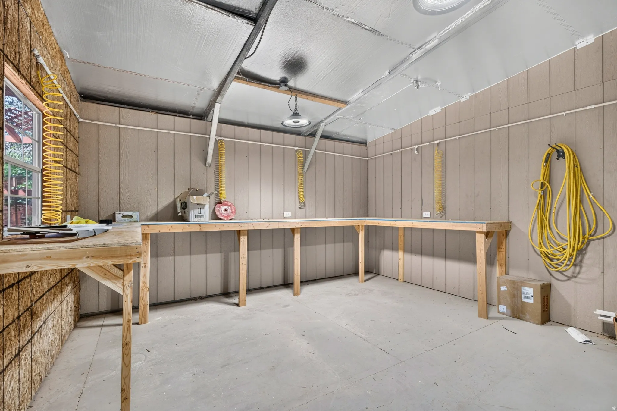 Dedicated workspace featuring extensive built-in wooden workbenches, concrete flooring, and vertical paneling