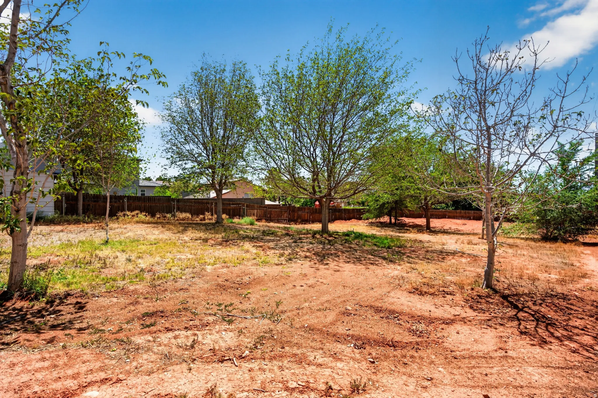 Spacious land parcel featuring mature trees, a partially wooded perimeter, and a surrounding privacy fence