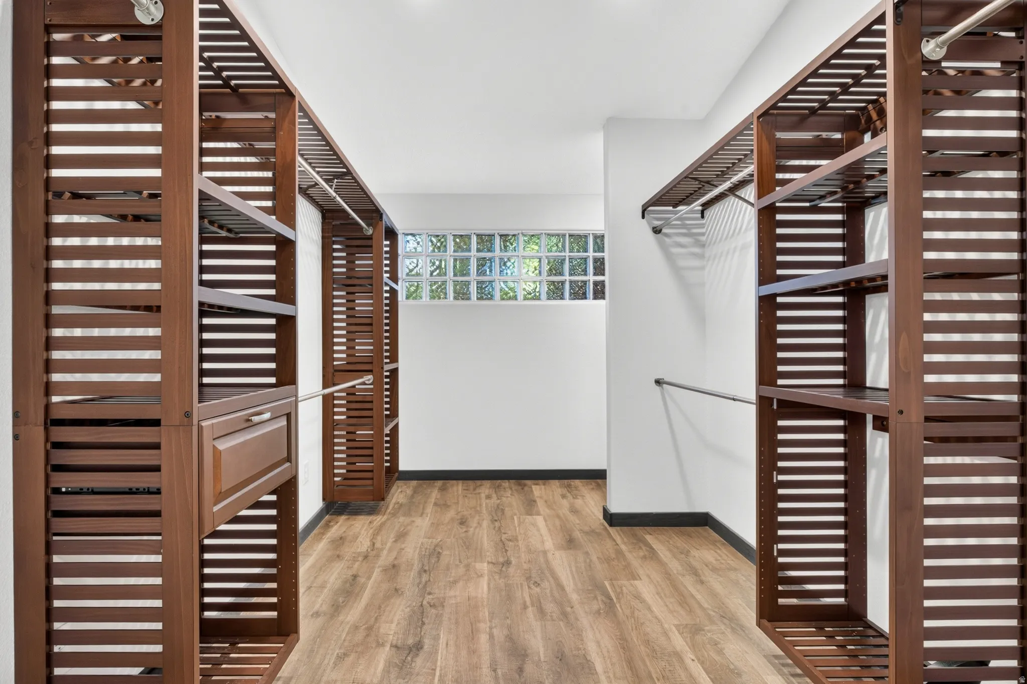 Spacious walk-in closet featuring extensive wood-finish shelving, integrated hanging rods, recessed lighting, wood-finish flooring, and a glass block window