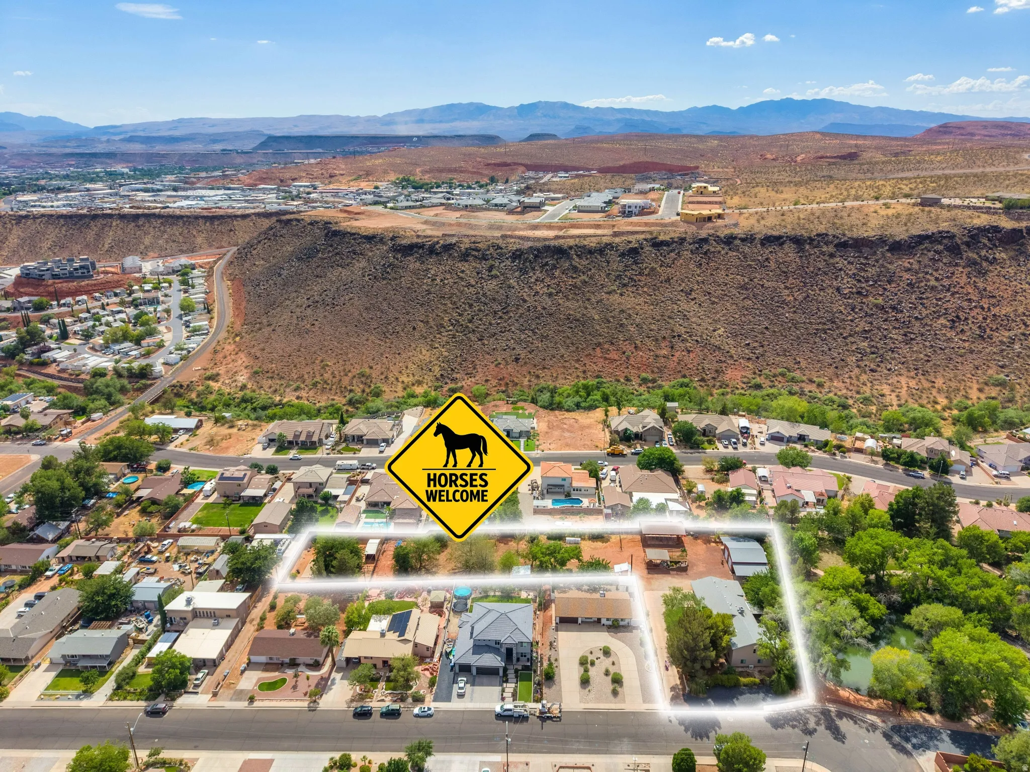 Aerial view of a residential area featuring multiple single-family homes, mature trees, and mountainous topography in the distance