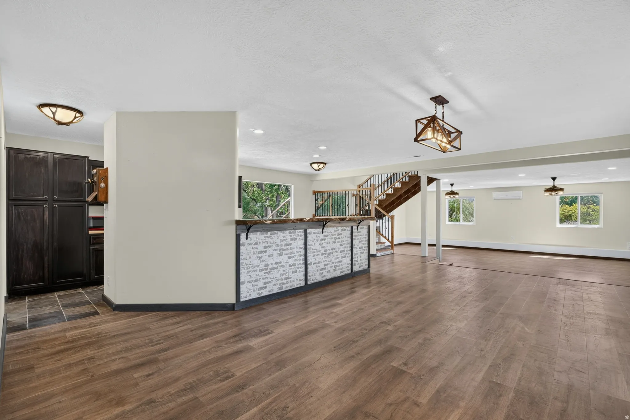 Spacious room featuring wood-finish flooring, a built-in bar with a decorative front, and a wooden staircase with railing