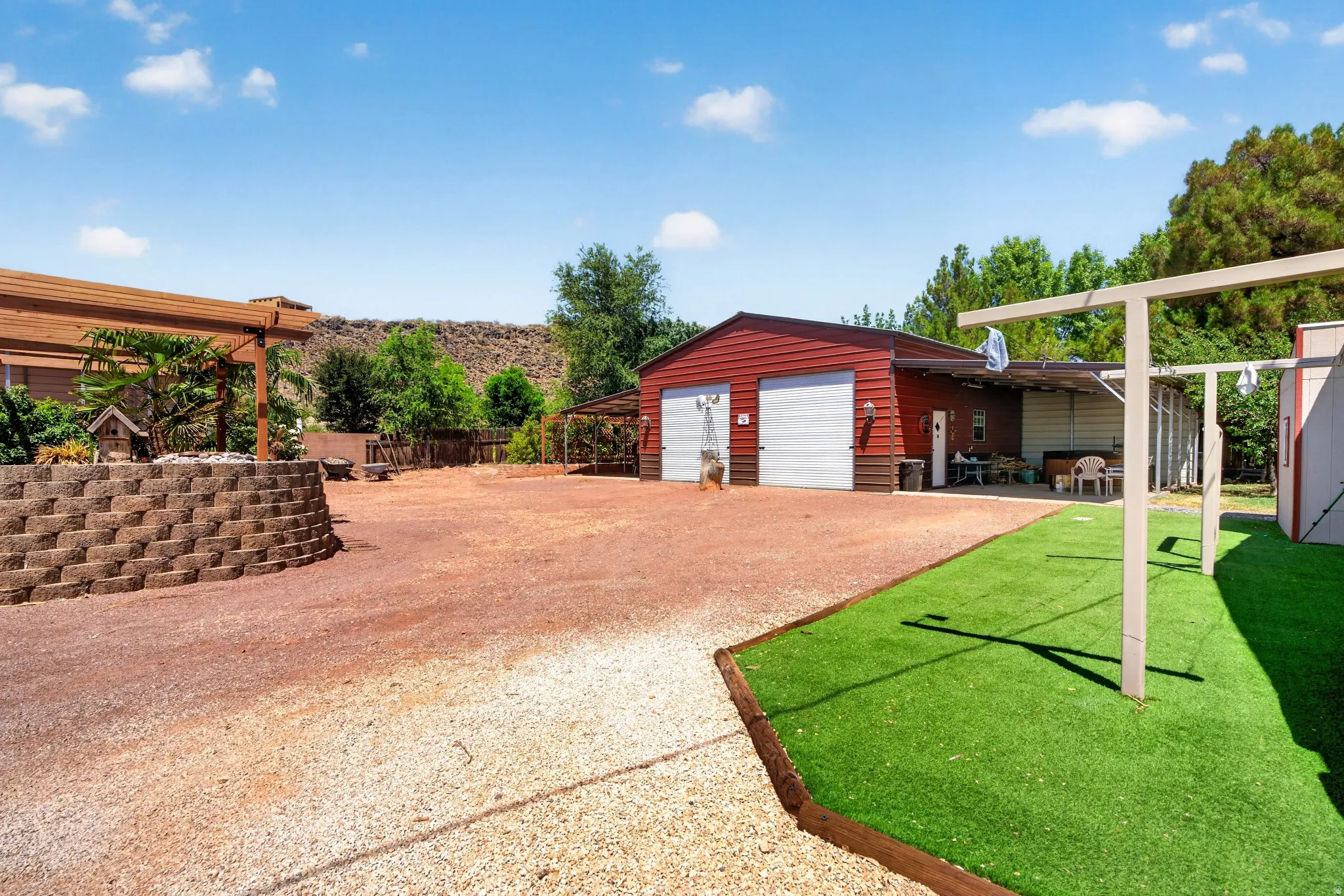 Spacious outdoor area featuring a two-bay detached garage, a large gravel driveway, and a section of artificial turf