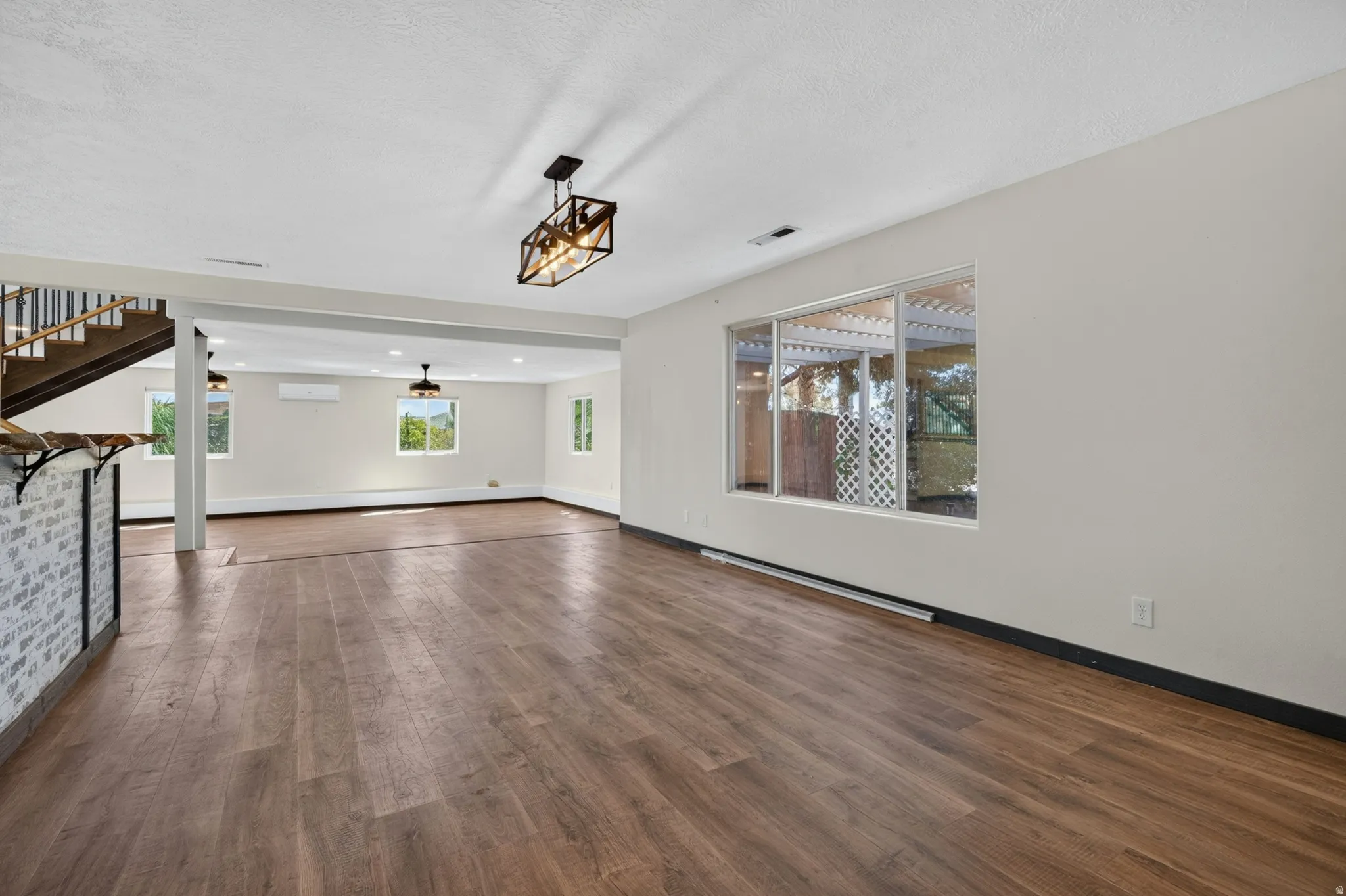 Spacious room with wood-finish flooring, white walls, and a large window overlooking an outdoor area