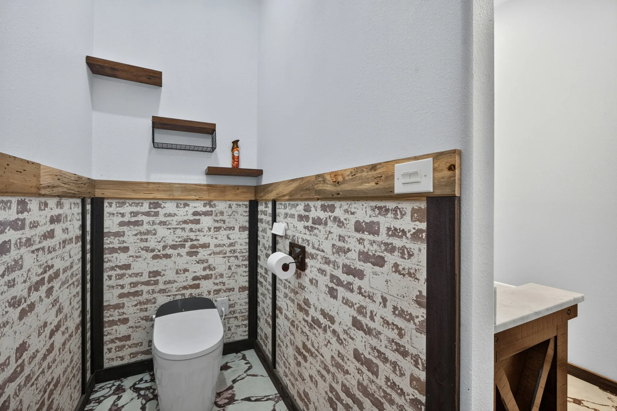 Powder room featuring a modern toilet, distressed brick-patterned wainscoting, light wood-finish trim, and coordinating floating shelves