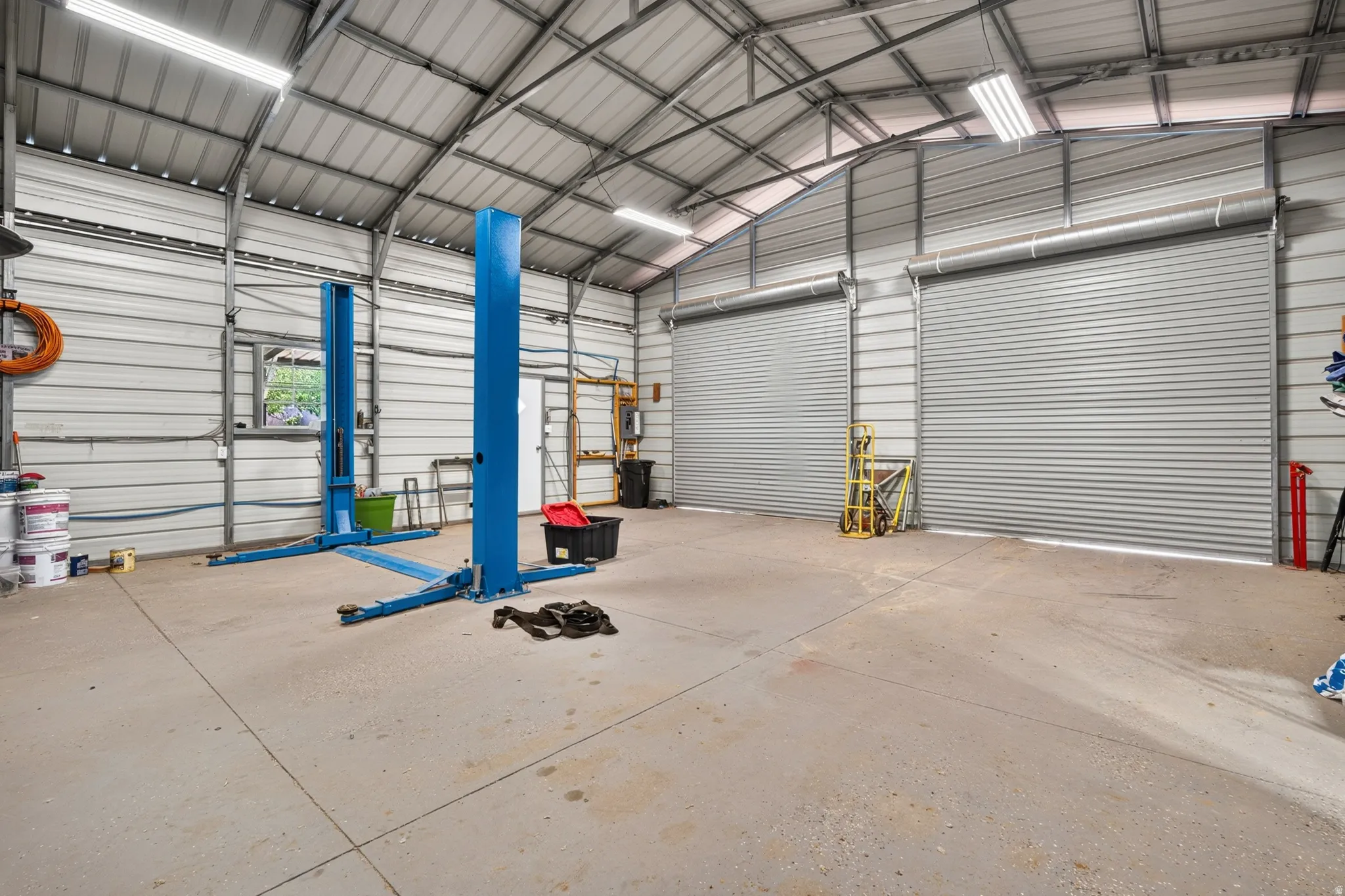 Spacious metal building interior featuring a concrete floor, two large roll-up doors, and overhead fluorescent lighting