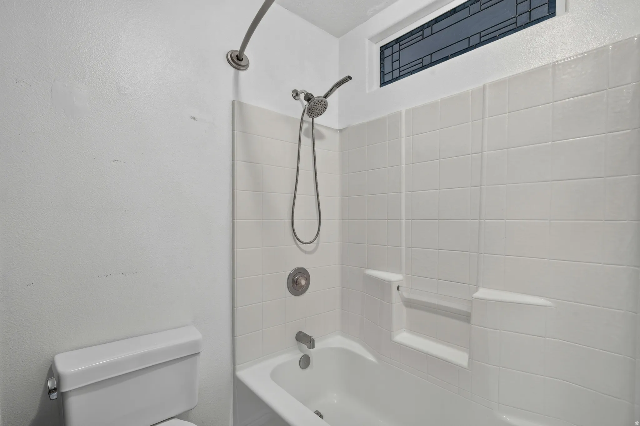 White tiled shower/tub combination featuring a brushed nickel showerhead and faucet