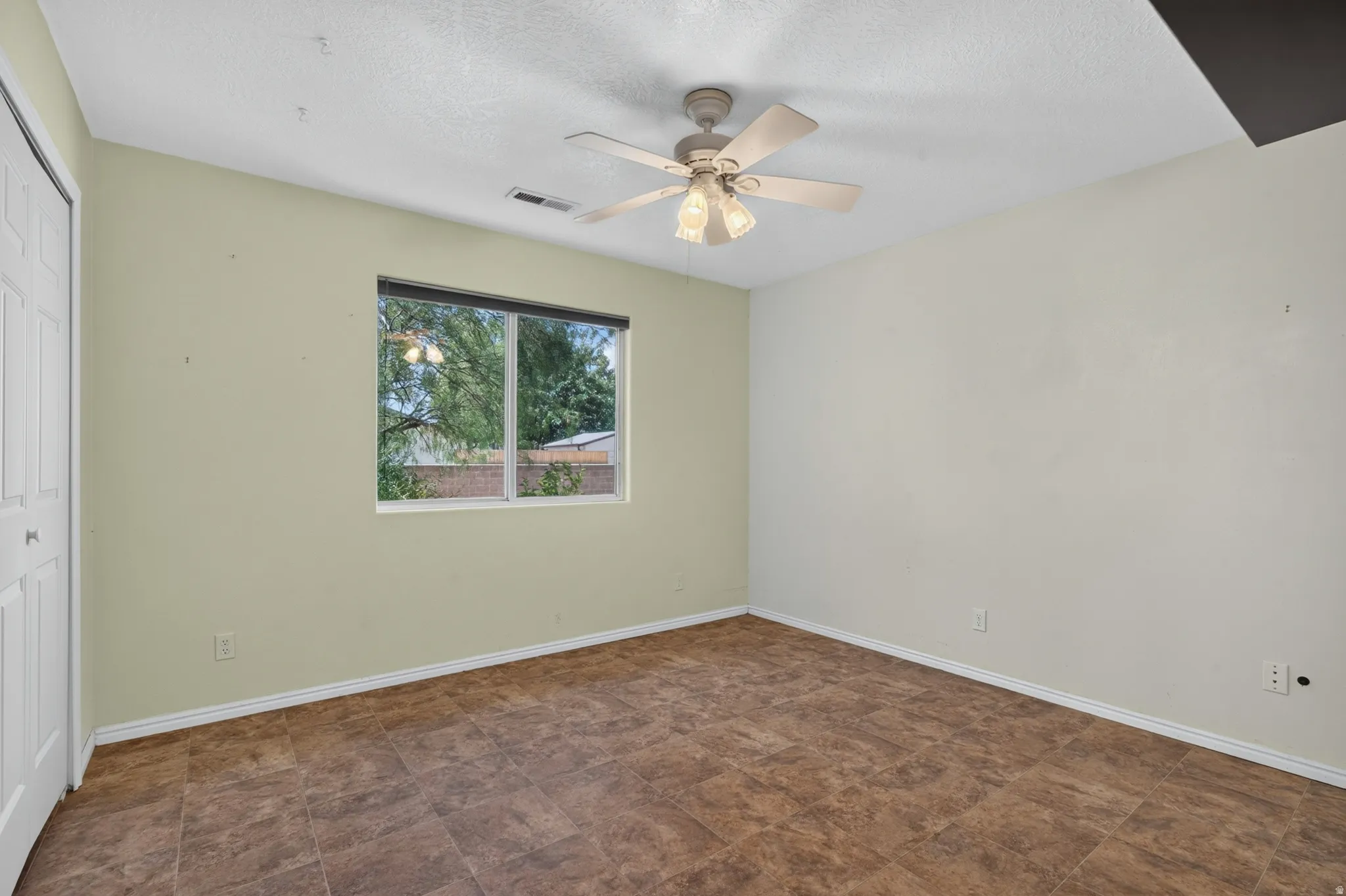 Room featuring a window, textured ceiling, ceiling fan with light fixture, and brown tile flooring