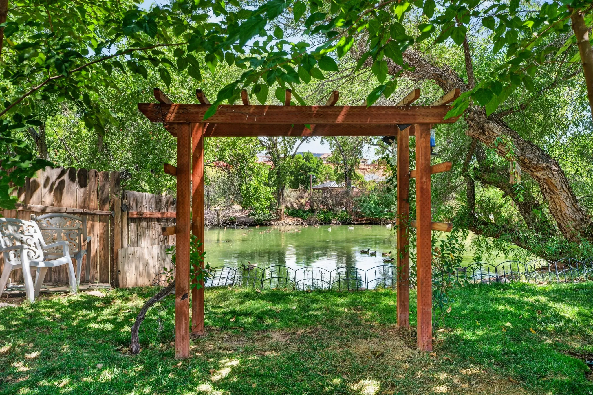Expansive green space featuring a wooden arbor, mature trees, and a body of water with a short decorative fence