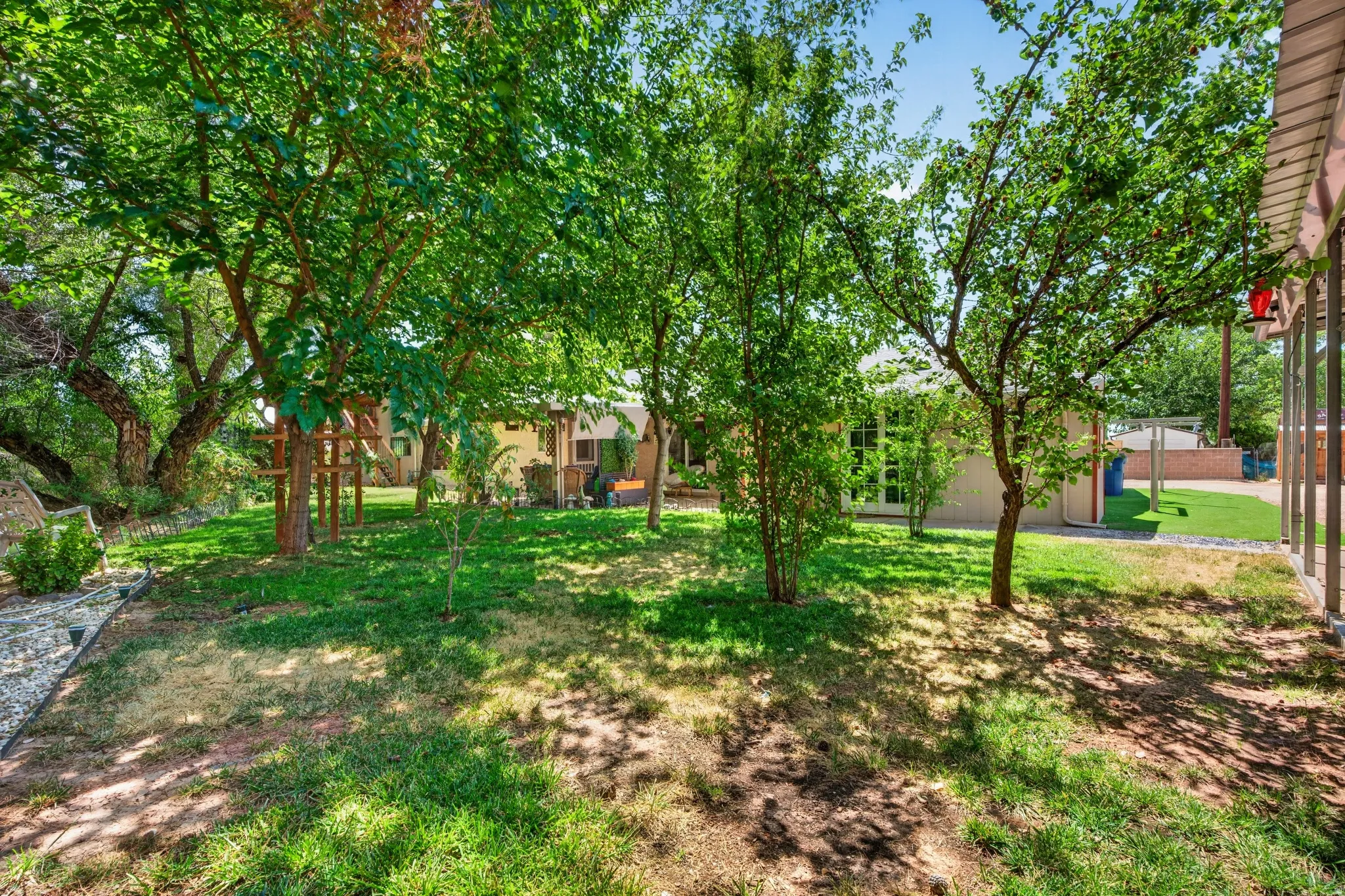 Expansive backyard featuring mature trees, a manicured lawn, and a light-colored exterior with large windows