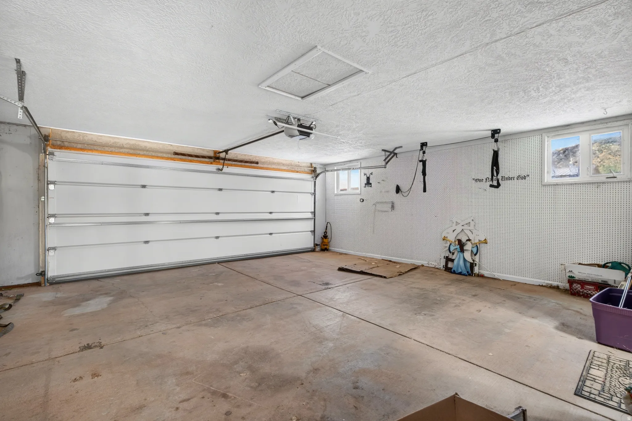 Garage featuring a segmented overhead door, concrete flooring, two windows, and textured wall paneling