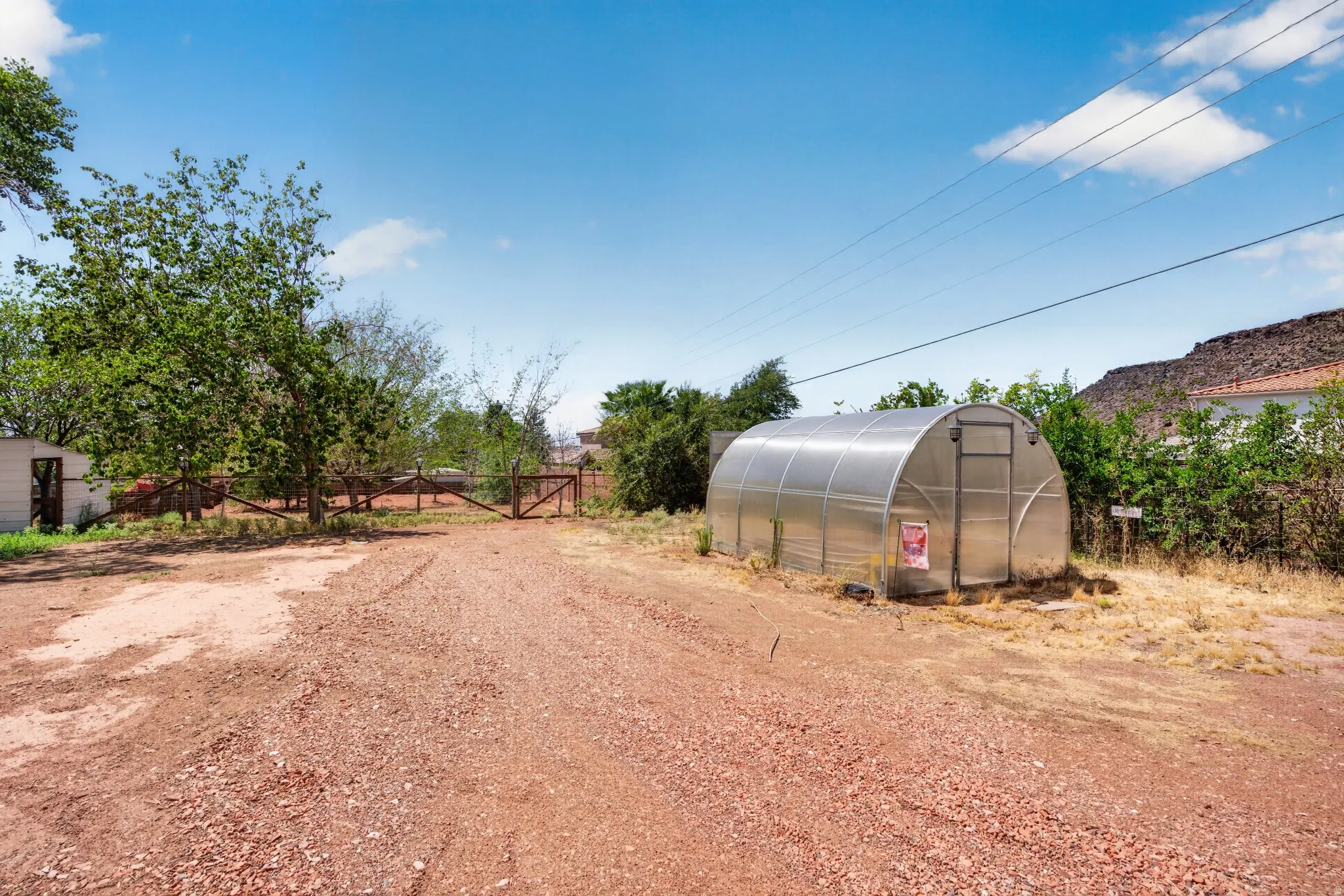 Arched greenhouse structure on a gravel lot with a wooden fence and gate
