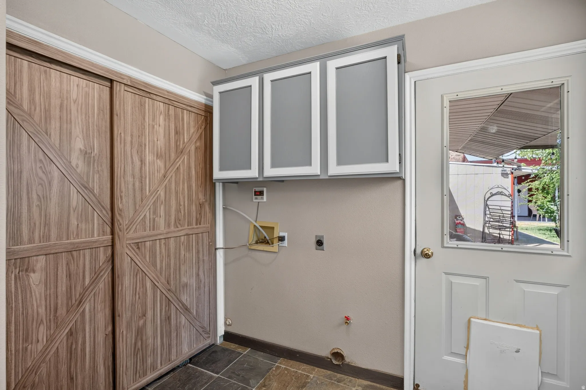 Laundry area featuring wood-finish sliding doors, slate-look floor tiles, and upper cabinetry with grey panels and white frames