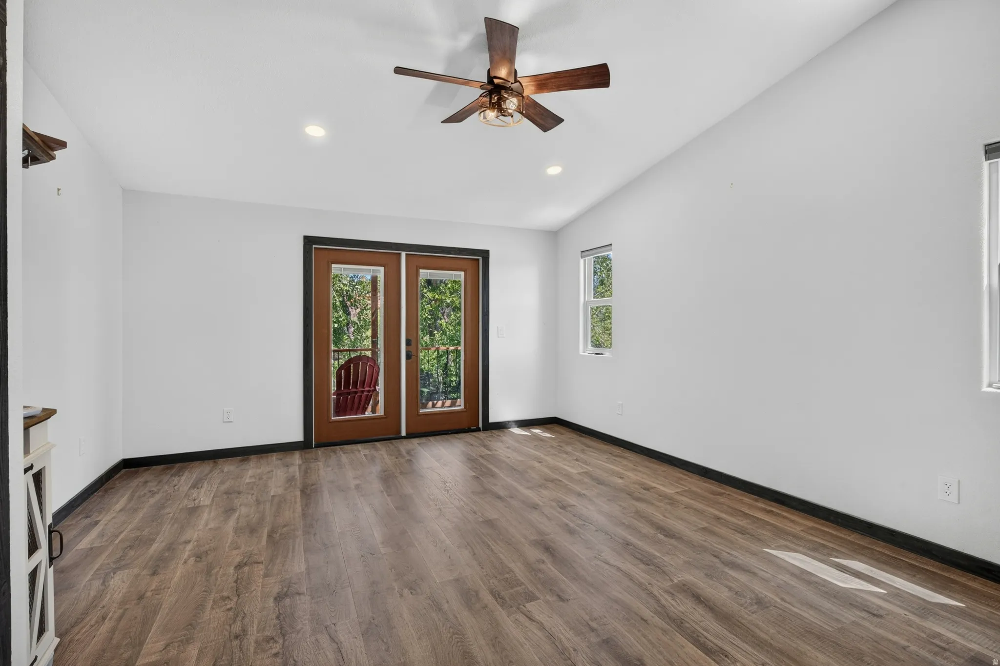 Spacious room featuring wood-finish flooring, vaulted ceilings, and a ceiling fan with integrated lighting