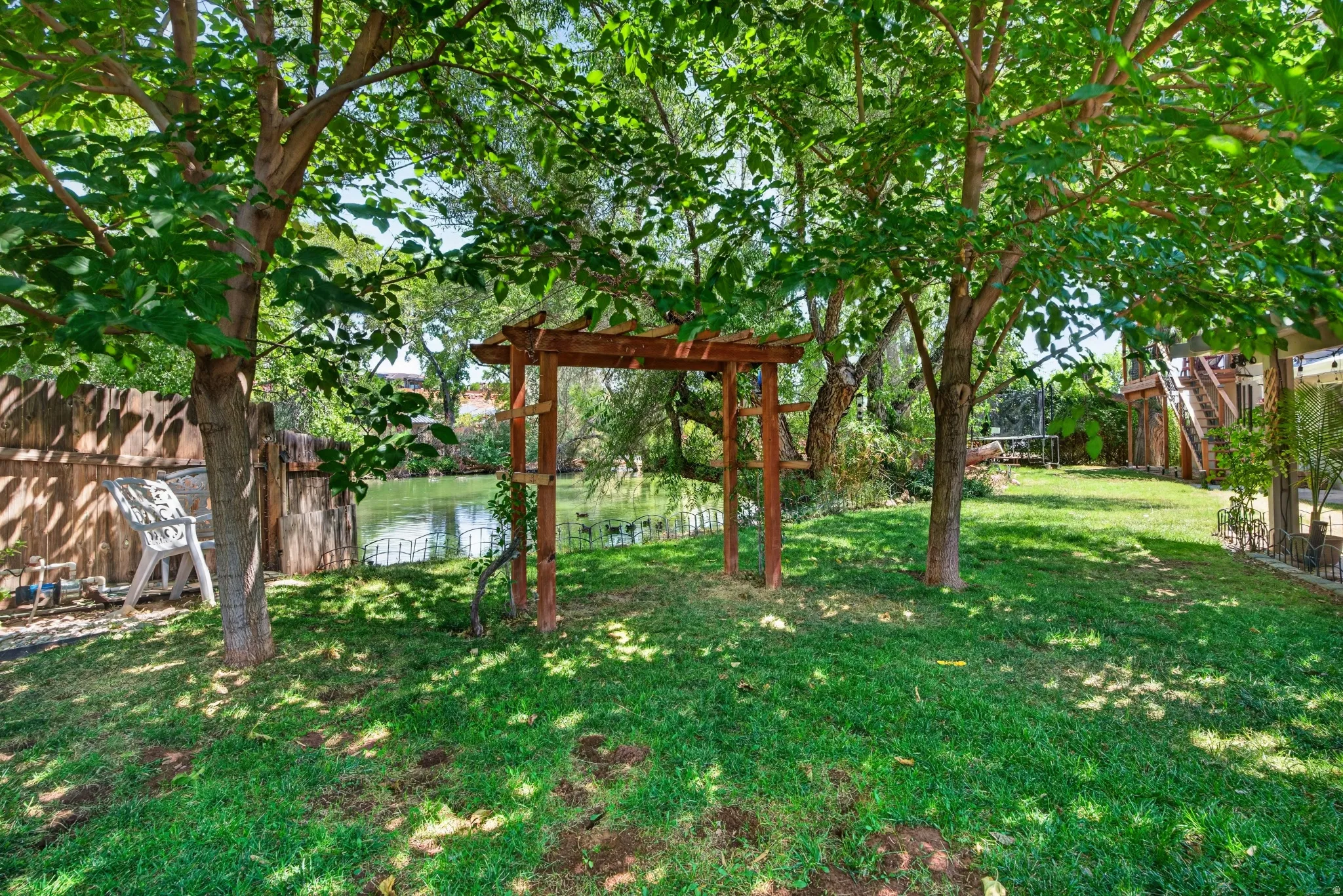 Expansive backyard featuring a lush lawn, mature trees, and a wooden pergola