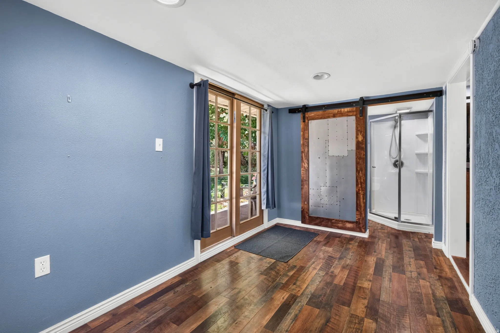 Interior space featuring wood-finish flooring, French doors, a modern barn door, and a corner shower enclosure